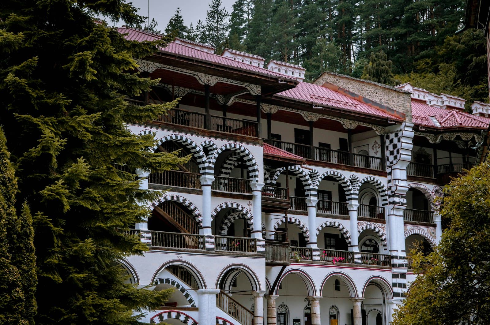 The striped black-and-white arcades and wooden balconies of Rila Monastery, set against a pine-forested mountainside