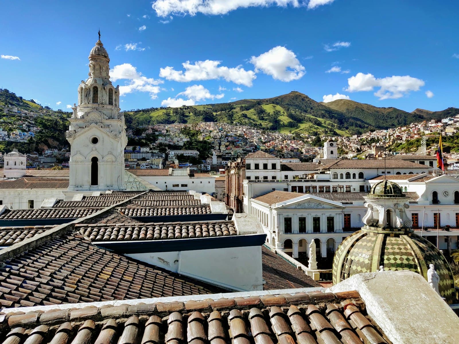 Terracotta rooftops and a white church bell tower in Quito's colonial old town, with green Andean hills behind