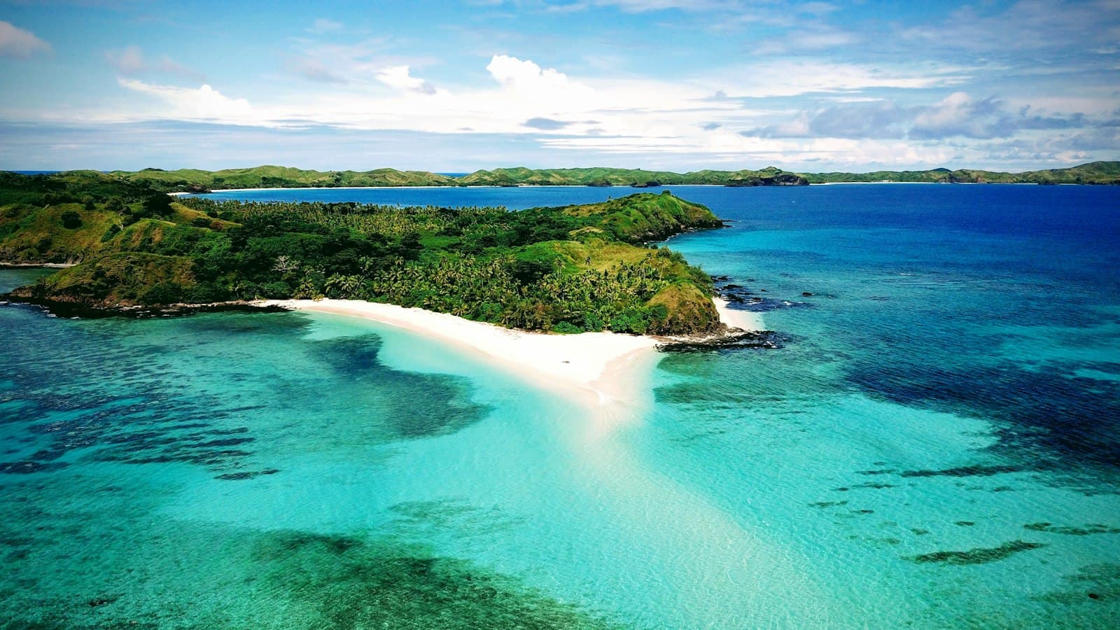 Aerial view of a palm-covered island with a white-sand spit reaching into a turquoise lagoon in Fiji