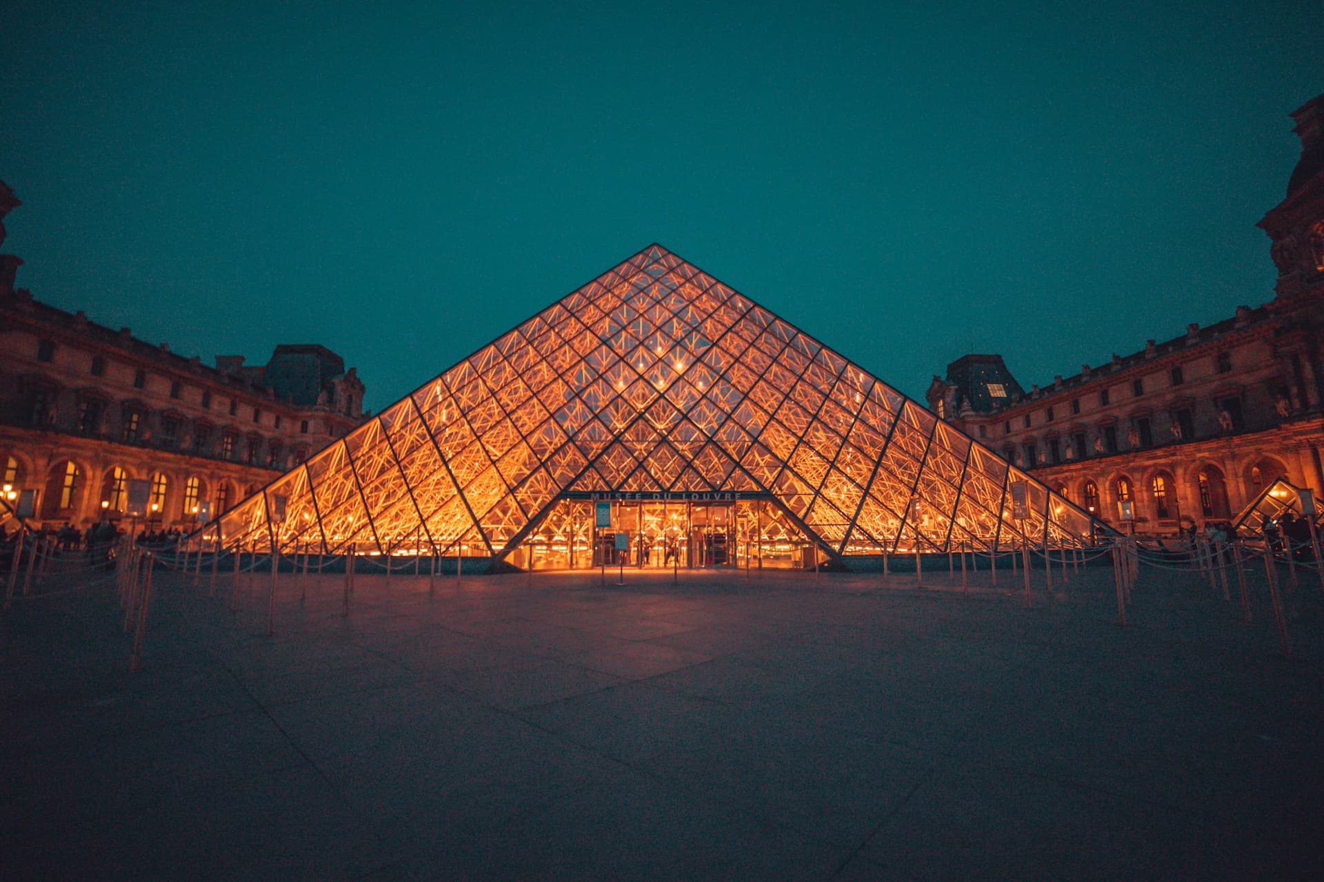 The Louvre Pyramid glowing at night against a teal sky, Paris