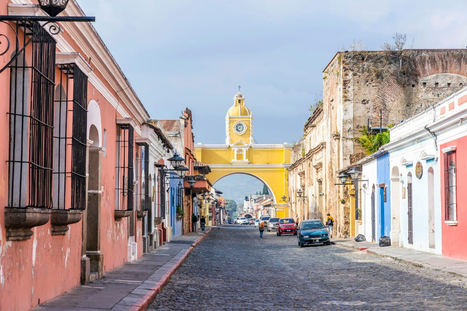 The yellow Santa Catalina Arch and clock tower at the end of a cobblestone street of colorful colonial houses in Antigua, Guatemala