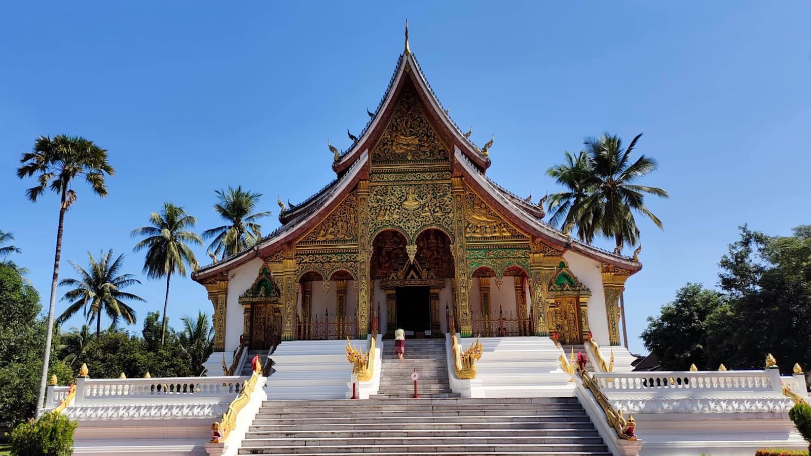 Gilded Buddhist temple with sweeping tiered roof framed by palm trees in Luang Prabang