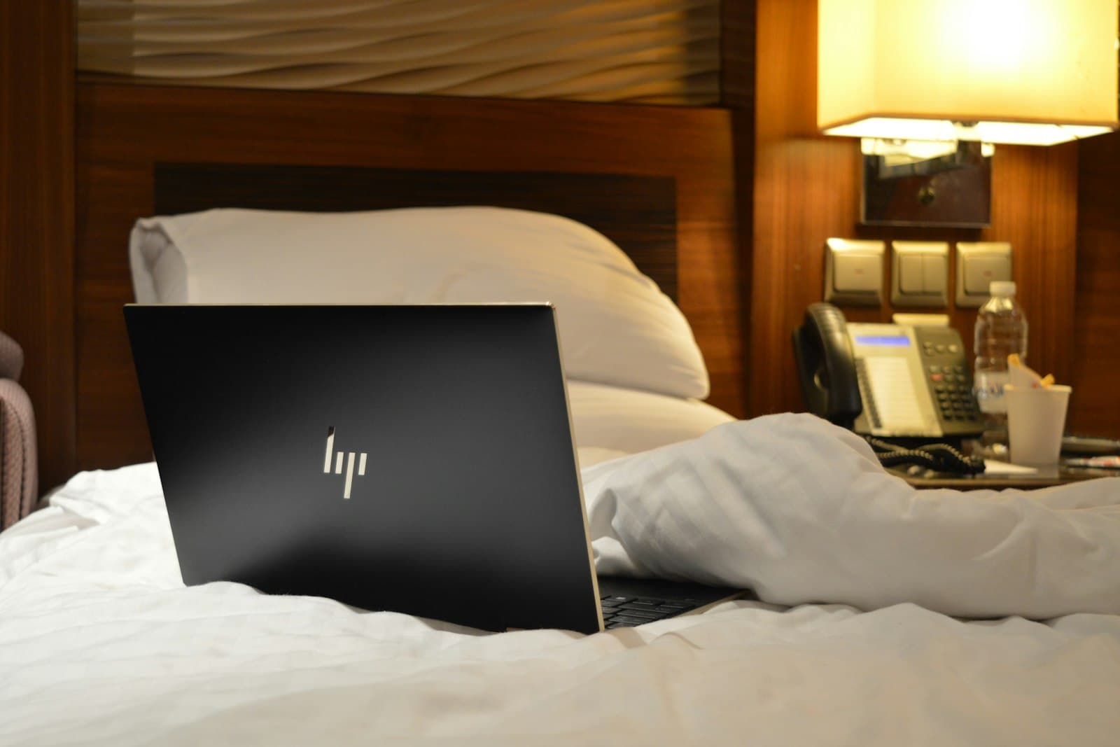 Laptop open on a hotel room bed — the working-traveler setup a travel router secures